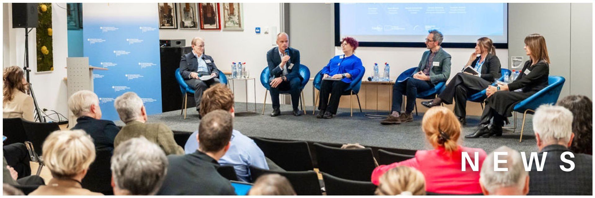 Six people discussing on a stage in front of an audience