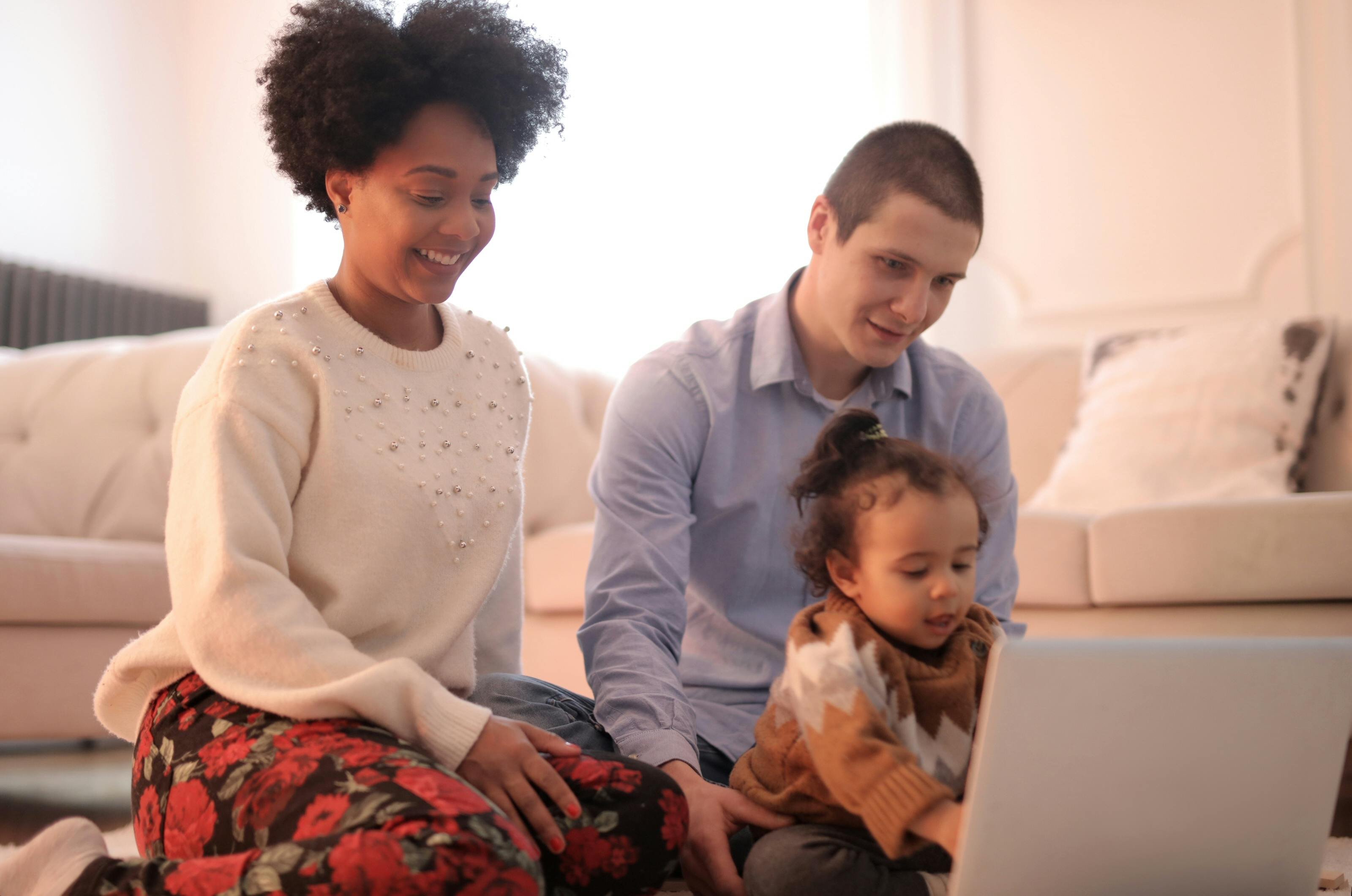 Young couple and a toddler sitting in their living room looking at a laptop together