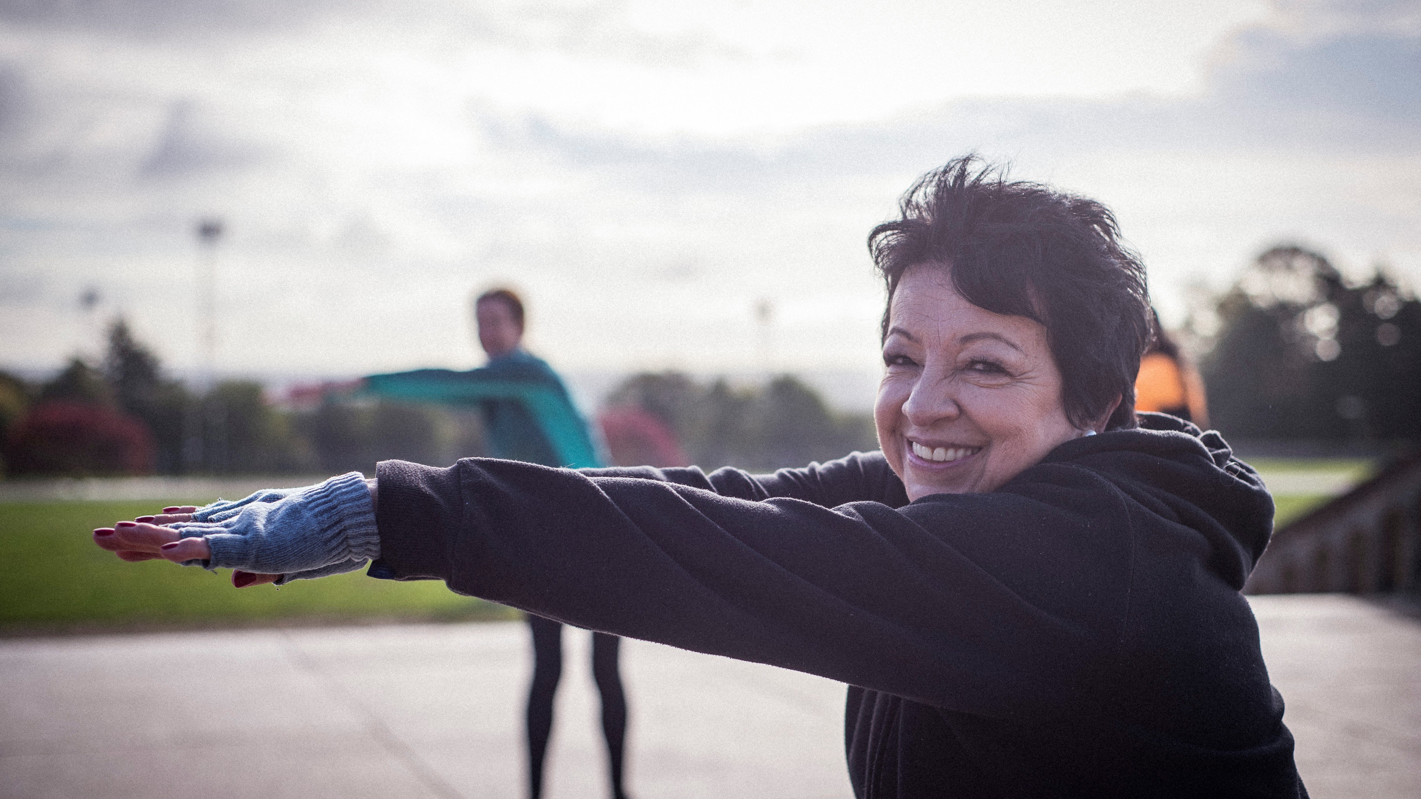 A women over sixty stretching outside, smiling
